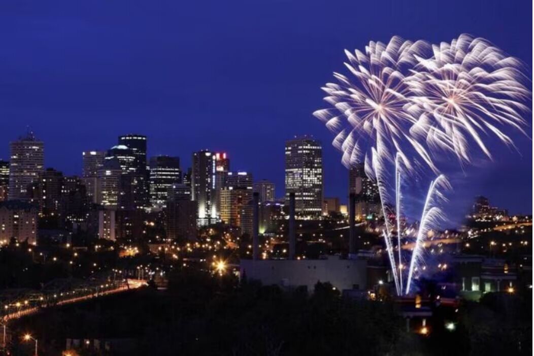 A city skyline with illuminated buildings and fireworks in the sky.