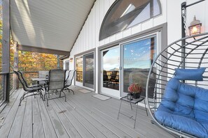 A covered outdoor deck with a table and chairs, a blue cushioned chair, and a view of the landscape through large sliding glass doors. - Luxury Mountain Retreat Game Room +Resort Access (Sapphire)