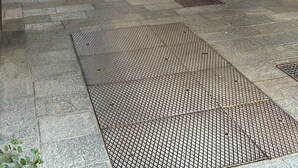 A gated entrance to a building with a metal gate, a doormat, and a paved area with a metal grate. - La Corte Guesthouse – Independent stay with private garden near Milan (Cornate d'Adda)