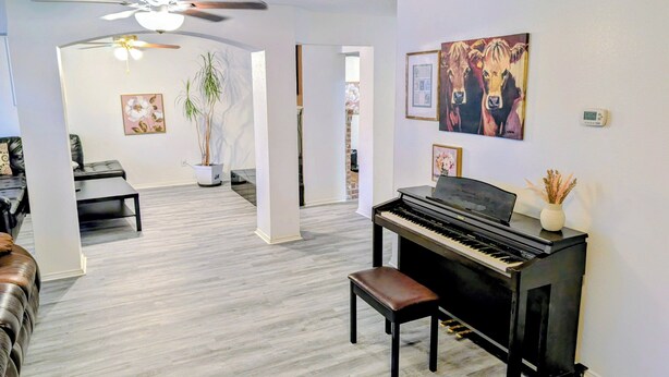 Un salon comprenant un piano, un canapé, une table basse, une plante en pot et un ventilateur de plafond.