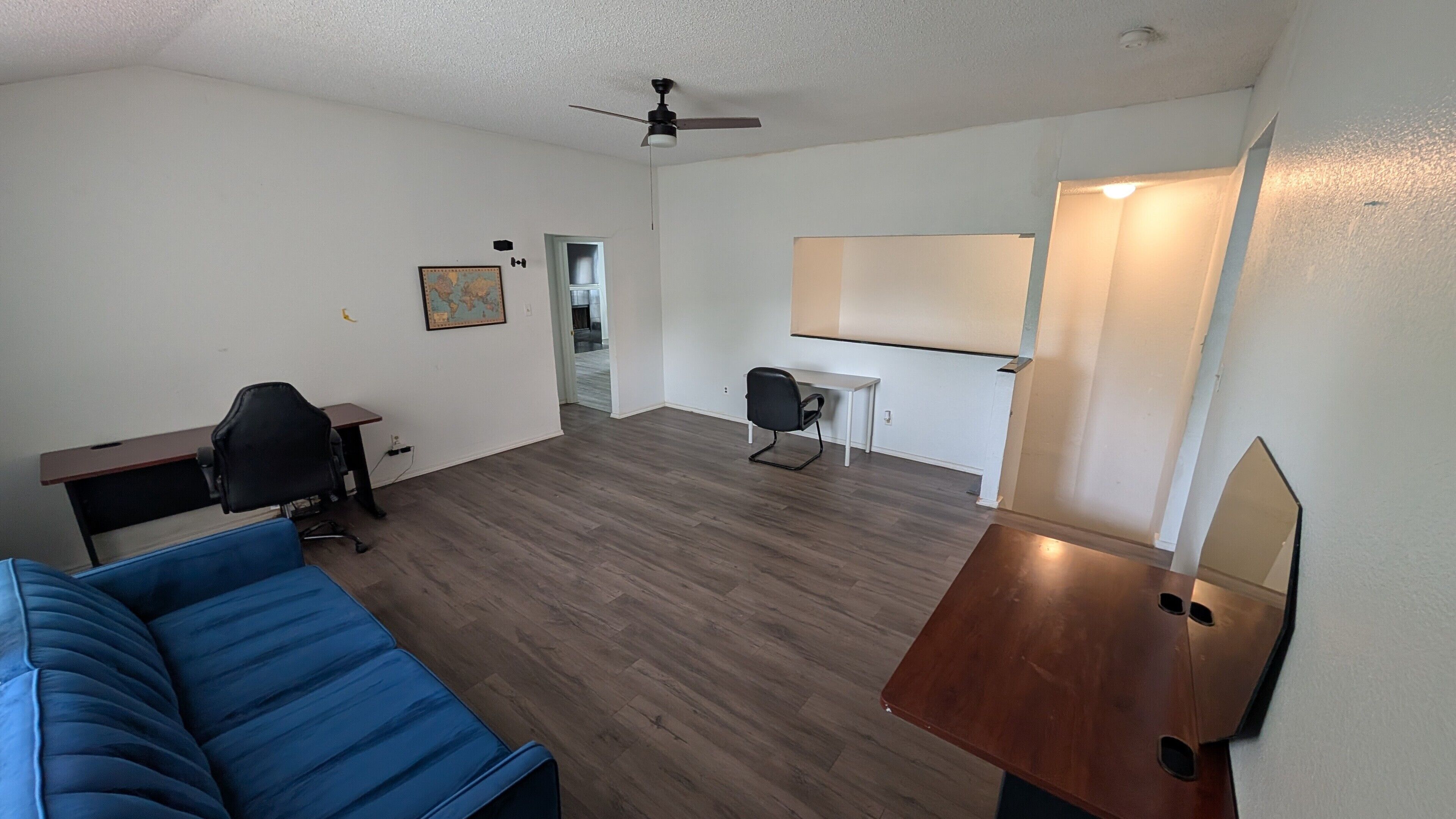 A room with a blue couch, a desk with a chair, a whiteboard, and a ceiling fan.