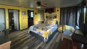 Une chambre à coucher comprenant un lit, un ventilateur de plafond, une fenêtre avec des rideaux et une porte donnant sur une salle de bain.