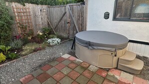 Un jardin avec un jacuzzi, une clôture en bois et un espace planté de différentes espèces végétales.