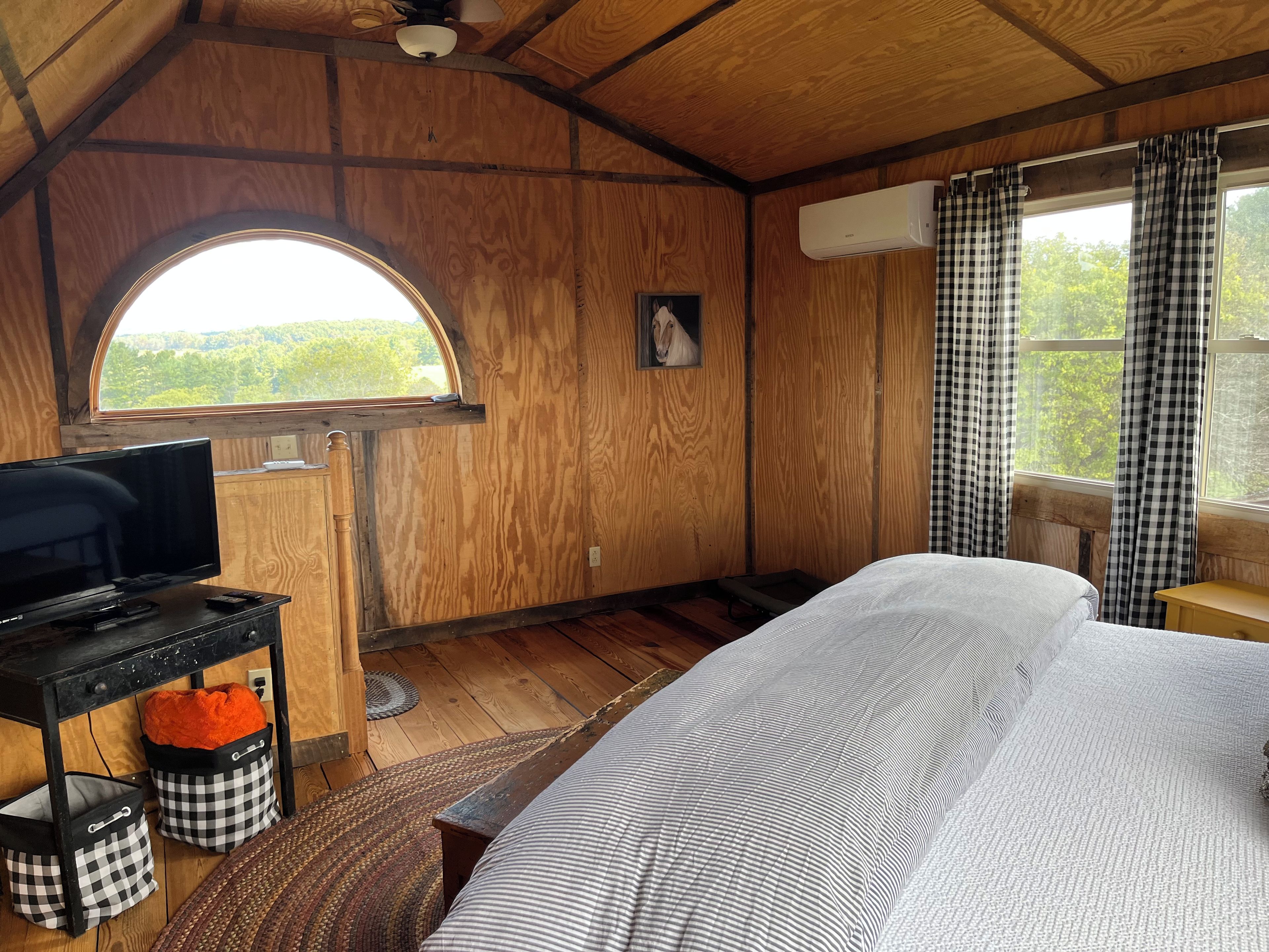 A room with a bed, a desk, a television, and a window with curtains.