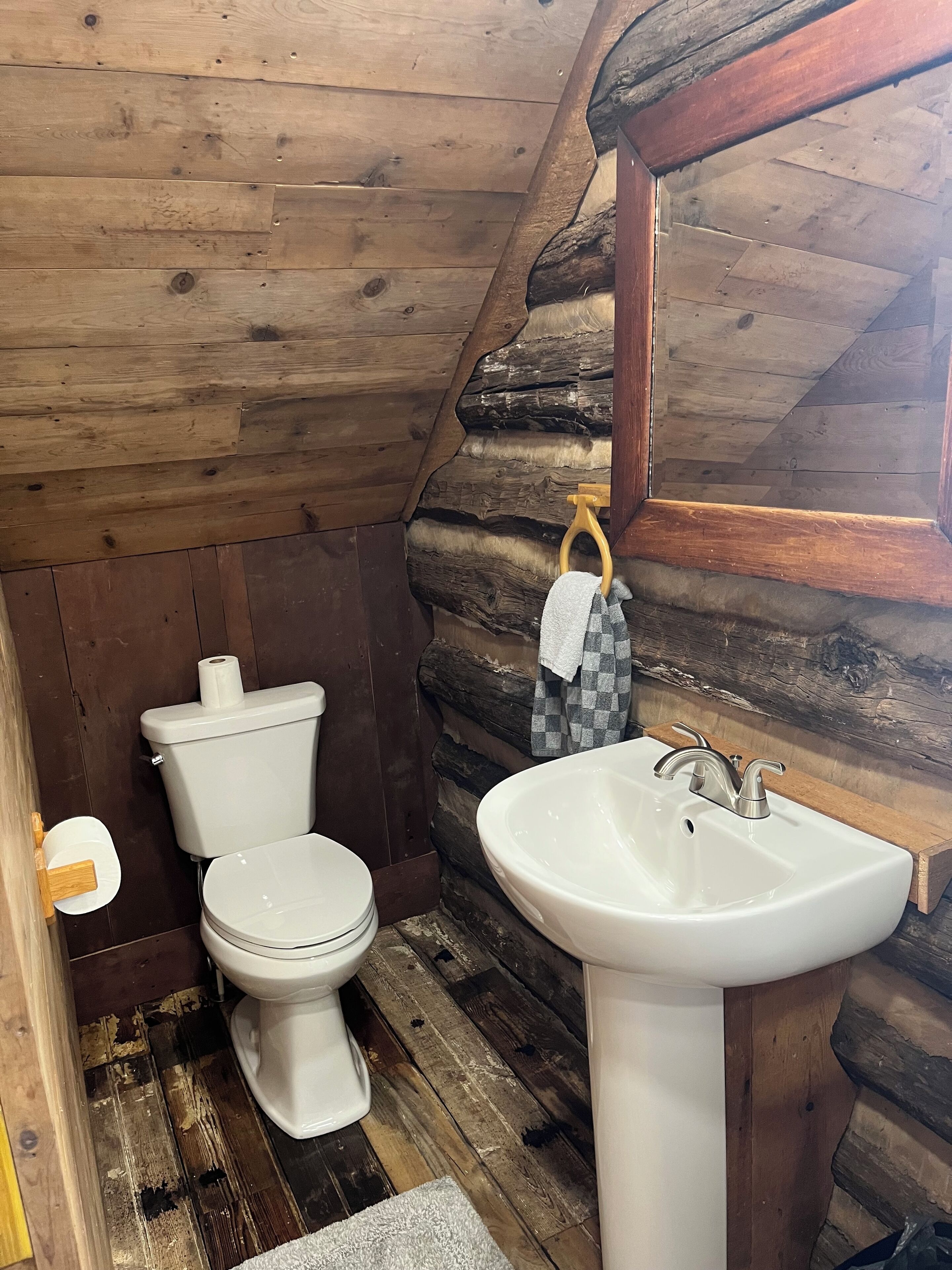 Un bagno rustico con parete in legno di tronchi, un water bianco e un lavandino bianco.