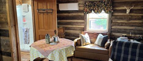 A cozy cabin interior with a wooden dining table, a sofa, and a window with a decorative skull.