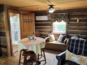 A cozy cabin interior with a wooden dining table, a sofa, and a window with a decorative skull.