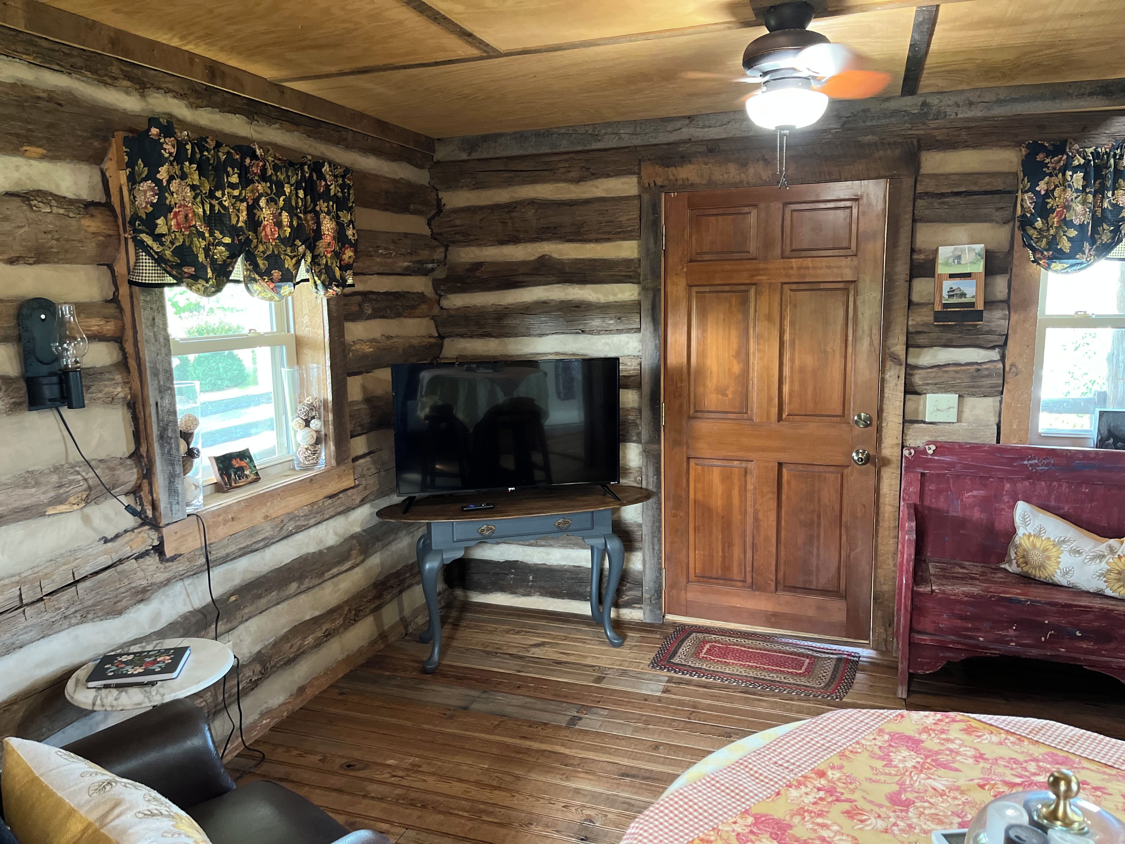A log cabin interior with a television on a wooden stand, a red sofa, and a wooden door.