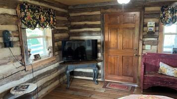 A log cabin interior with a television on a wooden stand, a red sofa, and a wooden door.