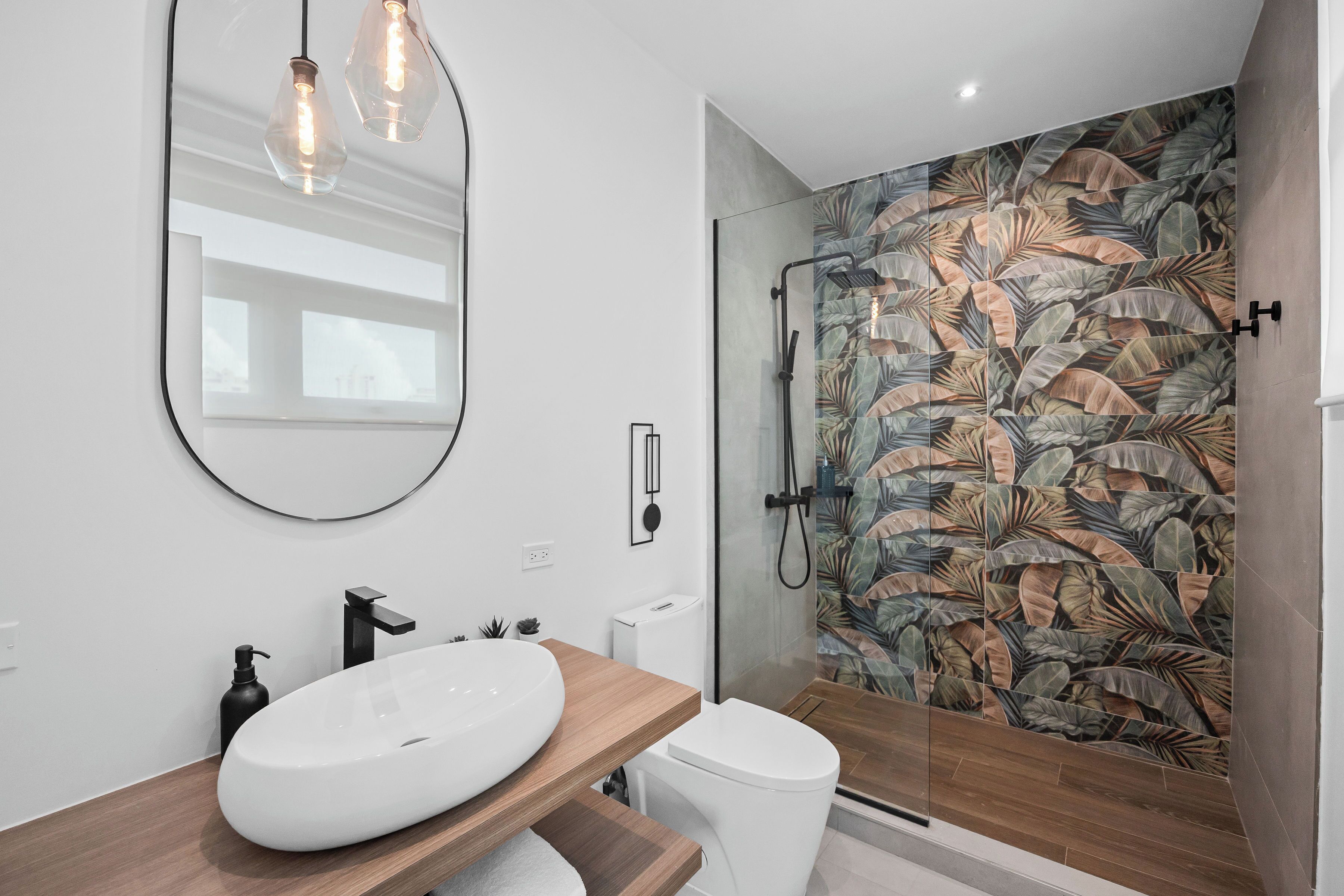 A modern bathroom with a large oval sink, a mirror, and a shower with a leaf-patterned wall.
