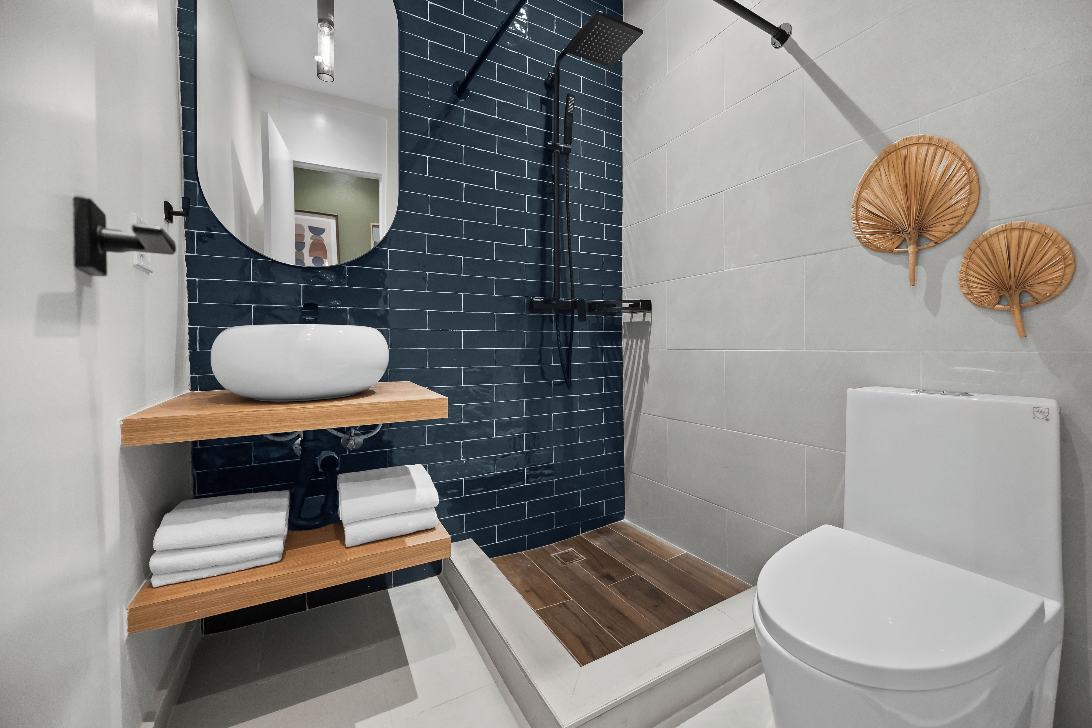 Un baño moderno con un lavamanos blanco, estantes de madera, un espejo y una ducha con cabecero negro.