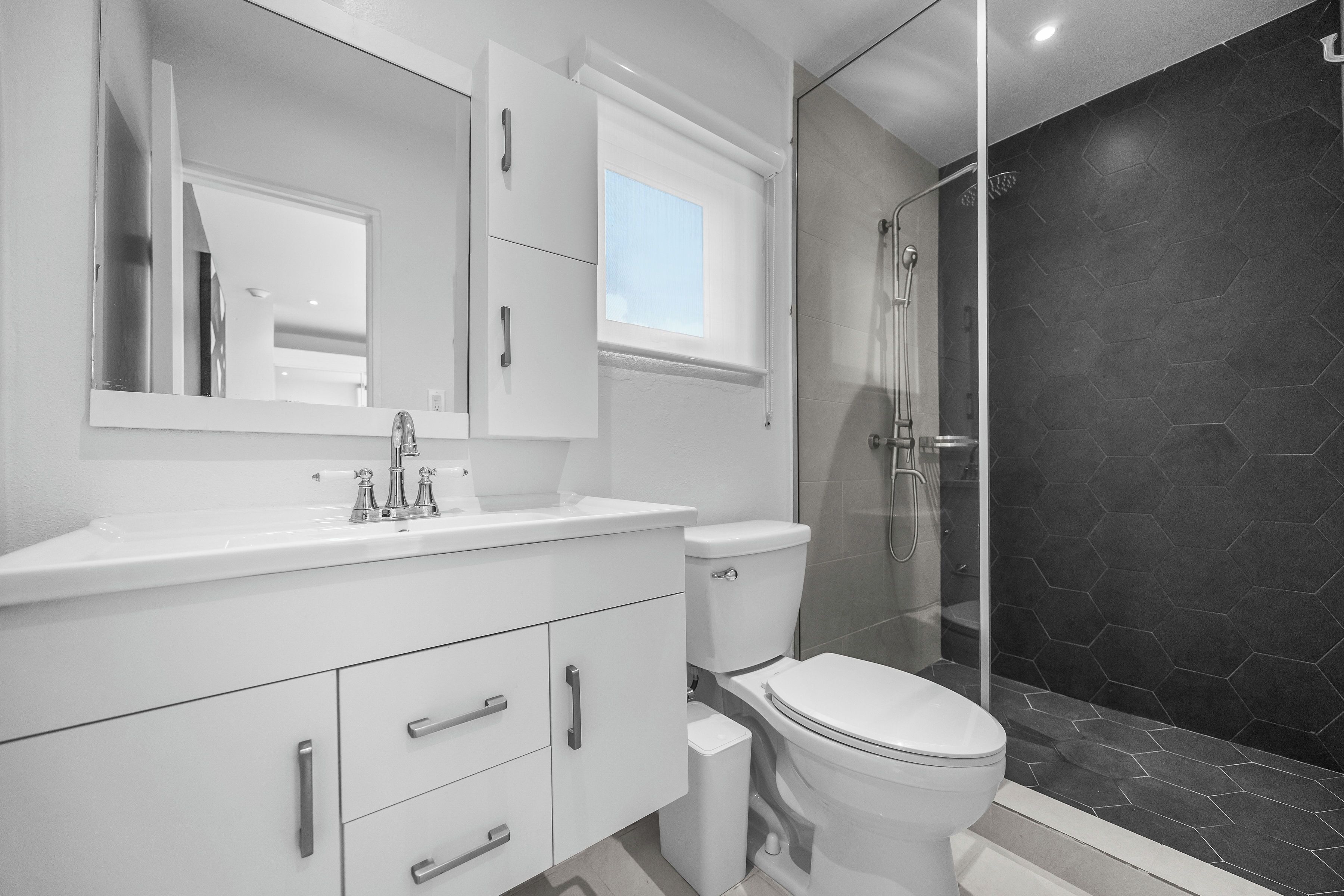 A modern bathroom with a white vanity, a toilet, and a glass-enclosed shower area.