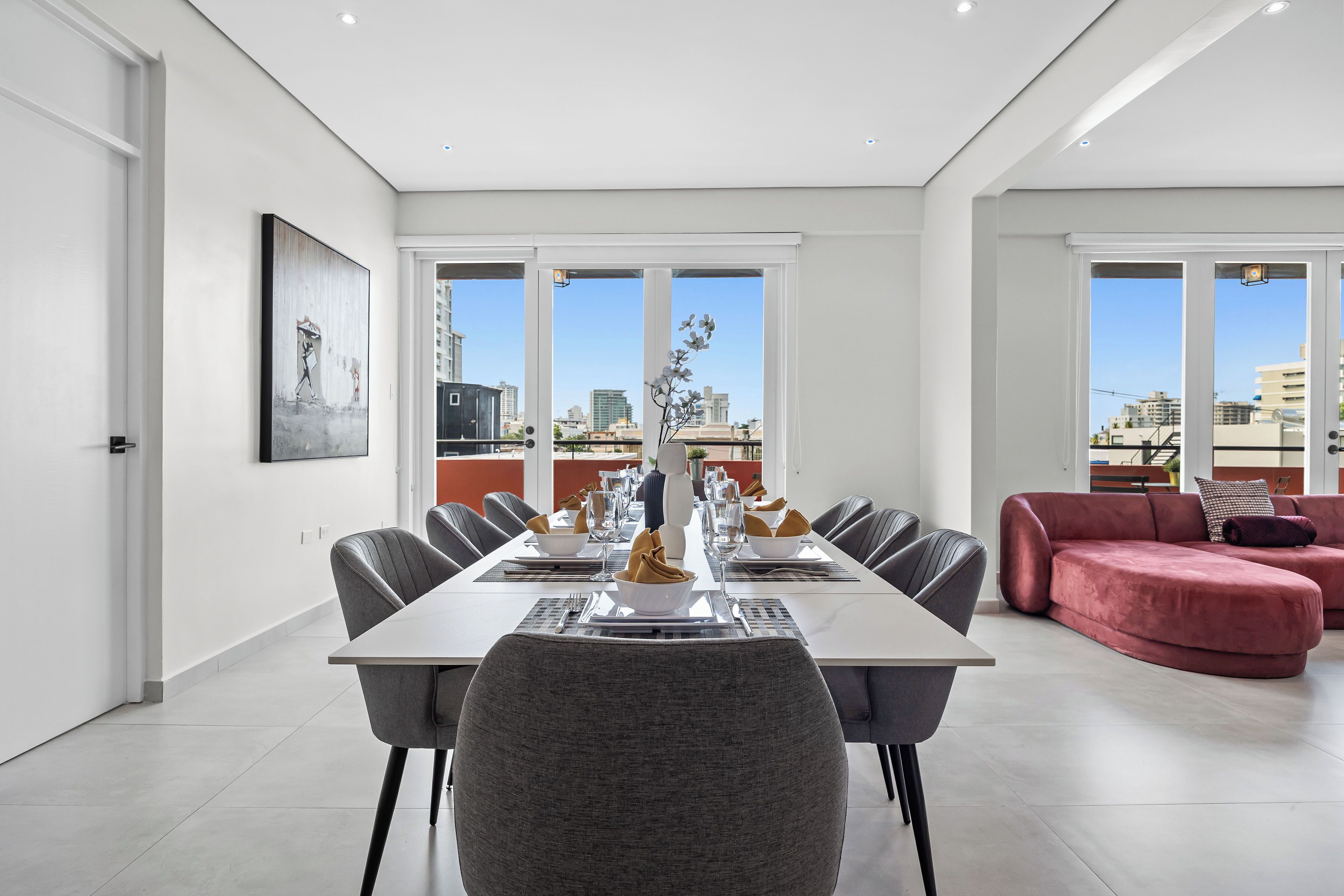 Uma sala de jantar moderna com uma mesa comprida, cadeiras cinzentas e um sofá vermelho.