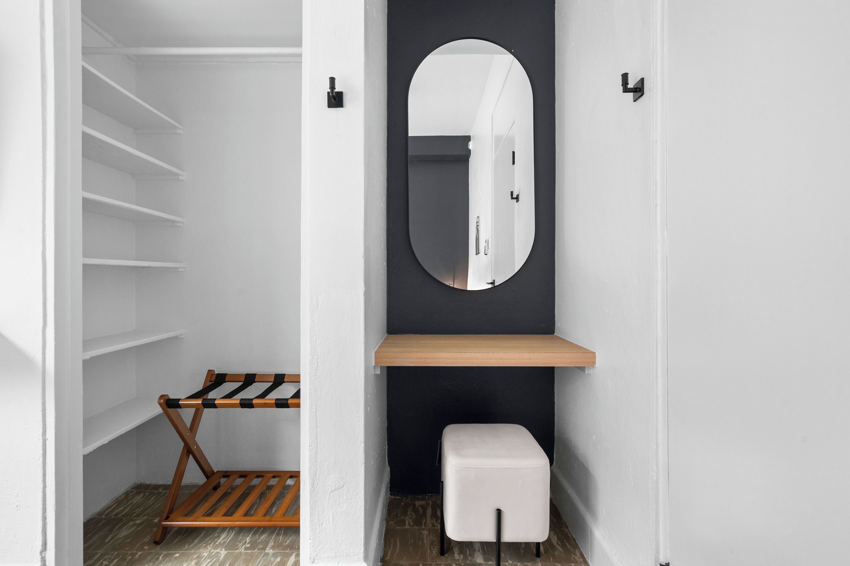 A walk-in closet with white shelves, a wooden bench, a mirror, and a small white stool.