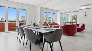 A modern dining area with a large table and chairs, a red sofa, and a city view through large windows. - Casa Placita Hotel (San Juan)