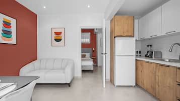 Eine moderne Küche mit weißen Schränken, einem Kühlschrank und einem Spülbecken. Im angrenzenden Raum befinden sich eine weiße Couch und ein Bett.