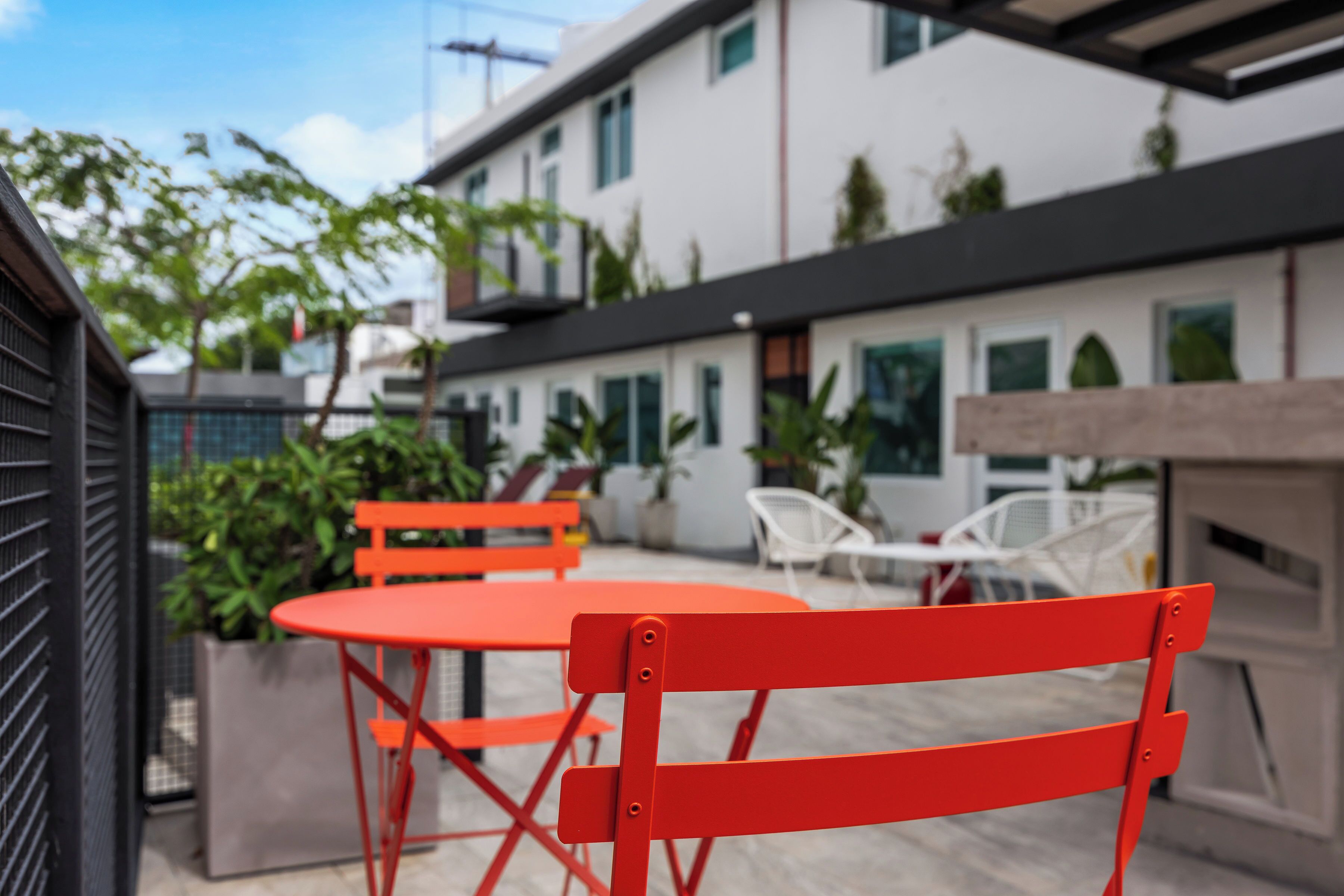 A modern outdoor seating area with red and white chairs, a table, and a building in the background.
