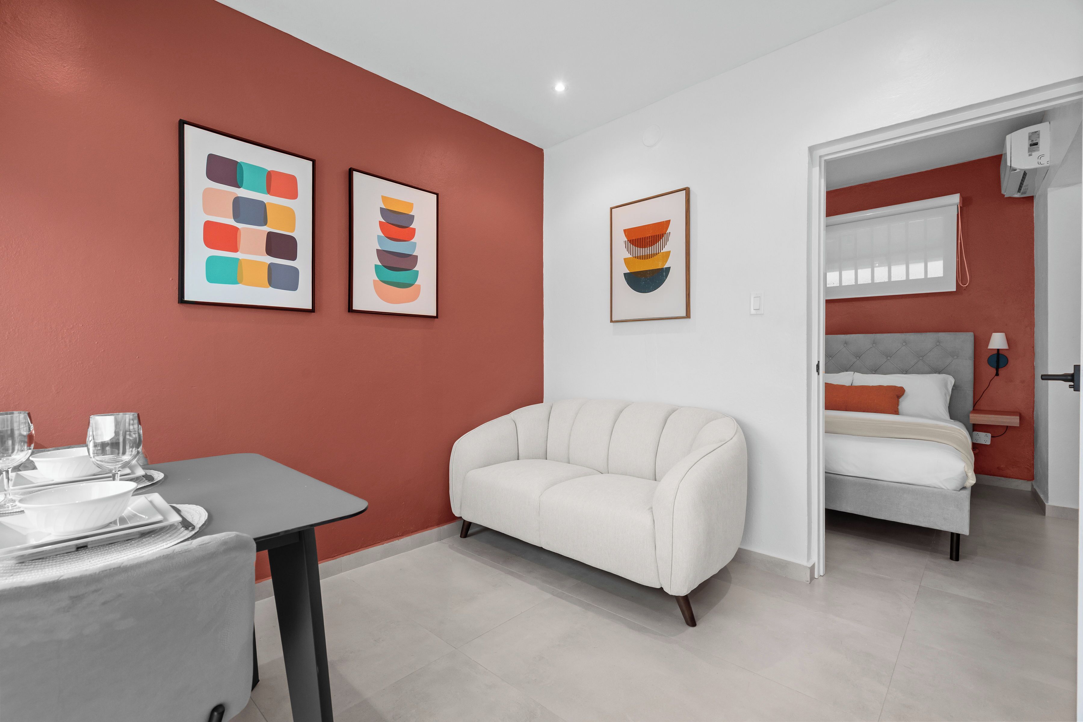 Una habitación moderna con un sofá blanco, una mesa de comedor con vasos y obras de arte en las paredes.