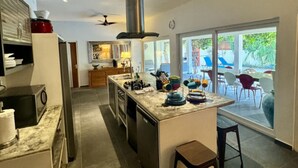 A modern kitchen with a central island, a built-in oven, and a large window overlooking a patio area. - 2BR ground level Villa at a TOP location with private Pool ! (Noord)