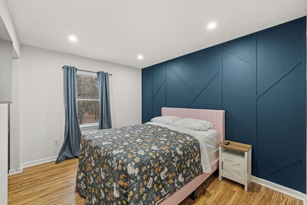 A bedroom with a bed, a nightstand, a window with curtains, and a blue accent wall. - Red Fox Den-Year Round Retreat At Massanutten- Ski, Bike, Golf, Hike & Waterpark (McGaheysville)