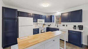 A modern kitchen with dark blue cabinets, white countertops, a wooden island, a white refrigerator, a microwave, and a coffee maker. - Red Fox Den-Year Round Retreat At Massanutten- Ski, Bike, Golf, Hike & Waterpark (McGaheysville)