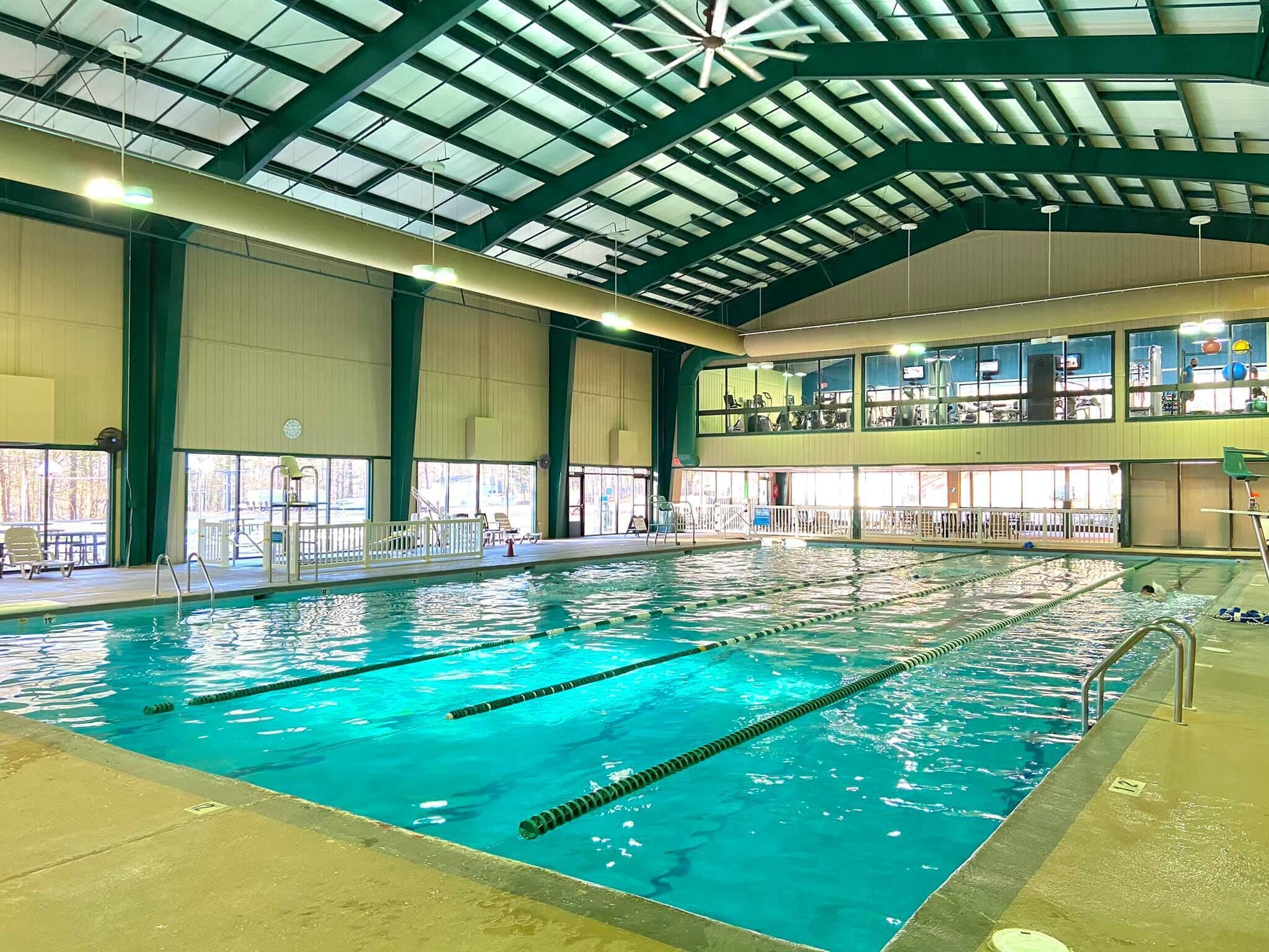 An indoor swimming pool with clear lanes, a high ceiling with skylights, and a view of the upper level with exercise equipment.