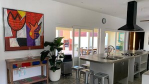 Una cocina moderna con una isla central, taburetes de bar, un cuadro abstracto grande y una planta en maceta.