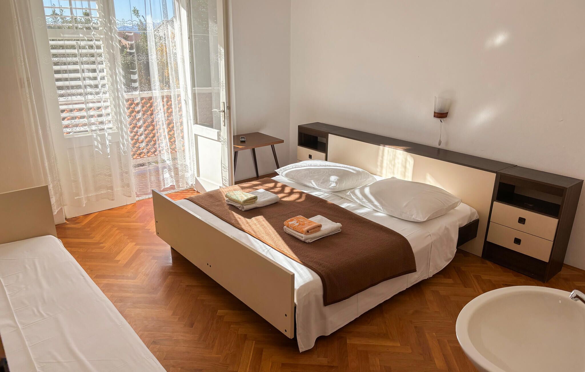 Habitación de hotel con cama, mesitas de noche, un escritorio pequeño, una silla y baño con lavabo e inodoro.