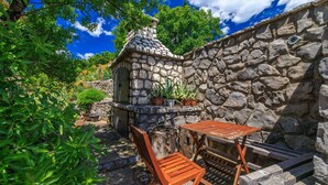 Un mur de pierres avec une petite construction en pierre, une table en bois et des chaises, le tout dans un cadre de jardin.