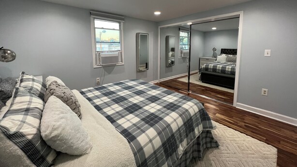 A bedroom with a bed, a window, a mirror, and a door leading to another room.