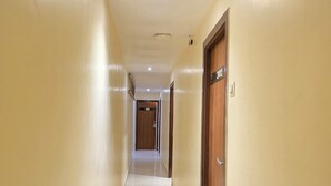 A corridor with cream-colored walls and a shiny tiled floor, leading to a door marked with the number 302. - Hotel Wellingten (Mumbai)