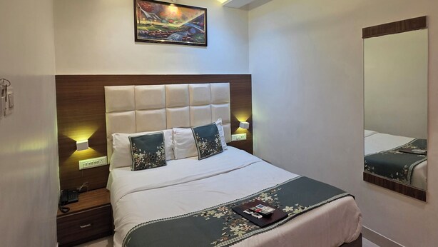 A modern bedroom with a large bed, a ceiling fan, recessed lighting, a painting, and a mirror. - Hotel Wellingten (Mumbai)