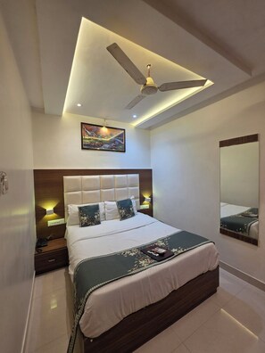 A modern bedroom with a large bed, a ceiling fan, recessed lighting, a painting, and a mirror. - Hotel Wellingten (Mumbai)