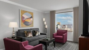 A hotel room with a grey sofa, a red armchair, a coffee table, and a large window with a city view. - Steps from the Las Vegas Strip Perfect Condo for National Rodeo Finals Event (Las Vegas)