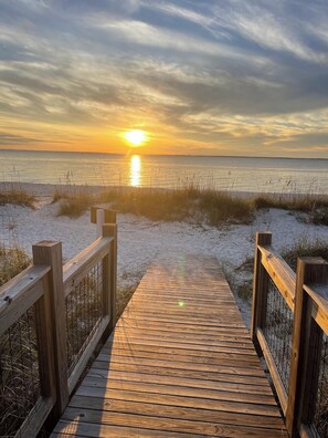 Un muelle de madera que conduce a una playa con un atardecer de fondo.