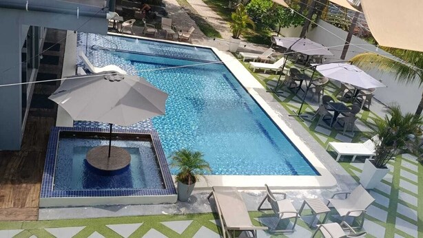 A rectangular swimming pool with lounge chairs and umbrellas, surrounded by greenery and a patterned floor. - Mi Tierra Surf City Hotel and Restaurant (La Libertad)