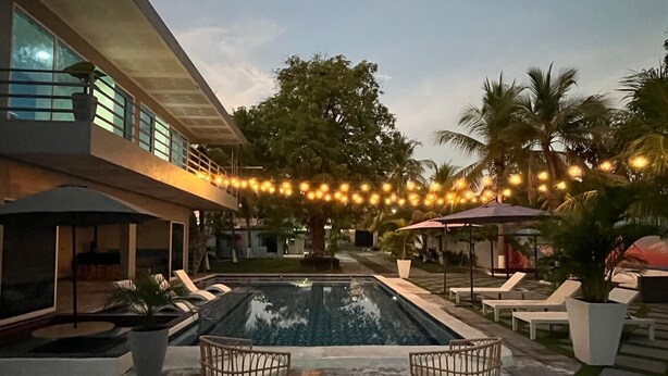 A pool area with lounge chairs, a swimming pool, and string lights. - Mi Tierra Surf City Hotel and Restaurant (La Libertad)