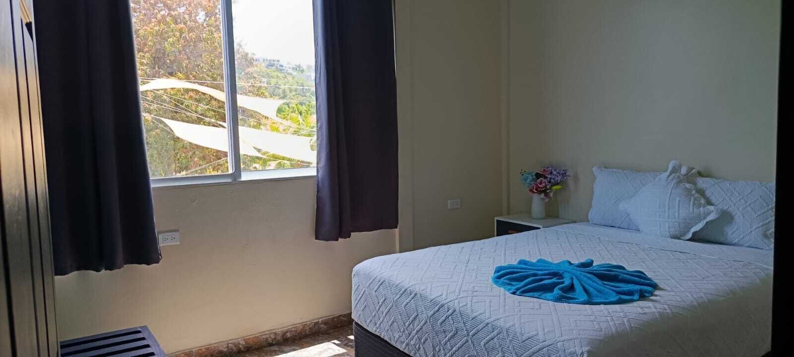 A bedroom with a bed, a nightstand, a window with curtains, and a view of greenery outside.