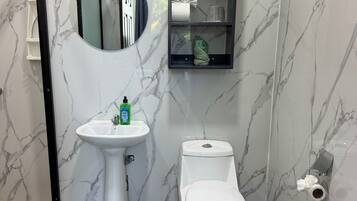 Een badkamer met een witte wastafel, toilet, spiegel en een plank met toiletartikelen.