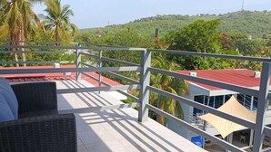 A balcony with wicker furniture, a red roof, and a view of a green hillside. - Mi Tierra Surf City Hotel and Restaurant (La Libertad)