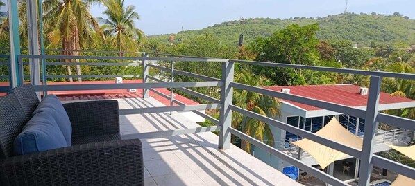 A balcony with wicker furniture, a red roof, and a view of a green hillside. - Mi Tierra Surf City Hotel and Restaurant (La Libertad)