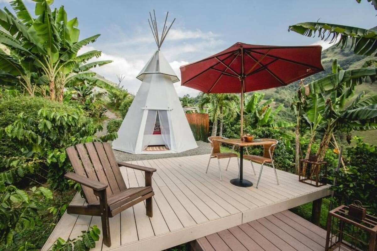 A wooden deck with a white teepee, a red umbrella, and a wooden chair.
