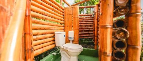 A bamboo-walled bathroom with a toilet and a handwashing station.