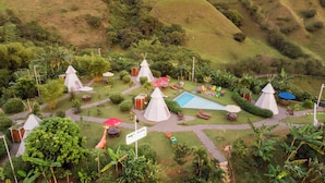 An aerial view of a resort with multiple conical huts, a swimming pool, and various outdoor seating areas surrounded by lush greenery. - Cerro Tusa Glamping  (Titiribí)