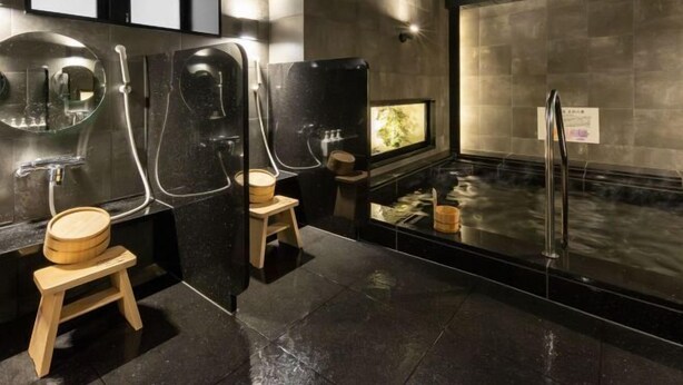 Ein modernes Badezimmer mit schwarzem Marmorboden, Holzschemeln und einer großen Badewanne mit einem Holzeimer.