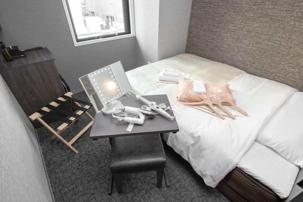 A hotel room with a bed, a desk with a laptop, a chair, and a window.