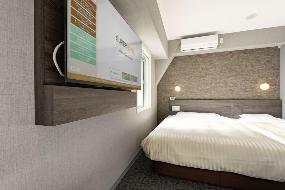 A hotel room with a bed, a mounted TV, and a wall-mounted air conditioning unit.