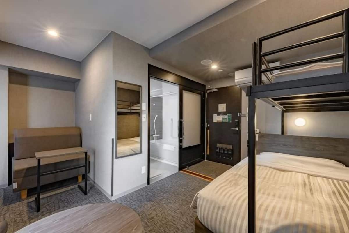 A hotel room with bunk beds, a sofa, a desk, and a sliding door closet.