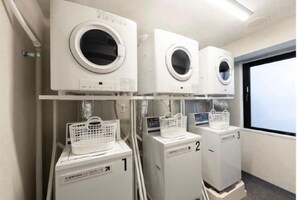 Egy mosókonyha, amelyben három mosógép és két szárítógép található, és mindegyik gép tetején egy-egy kosár van.