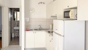 Eine moderne Küche mit weißen Schränken, einer Spüle, einem Wasserkocher, einer Mikrowelle und einer Uhr an der Wand.